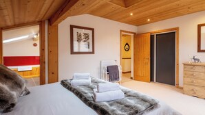 A bedroom with a bed, a fur throw, a wooden dresser, and a door leading to another room. - Morzine chalet with hot tub. Ski and MTB friendly (Montriond)