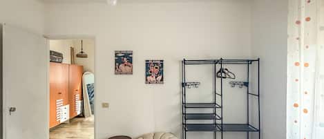 A bedroom with two beds, a hanging light, a wardrobe, a bean bag chair, and a metal shelf unit.