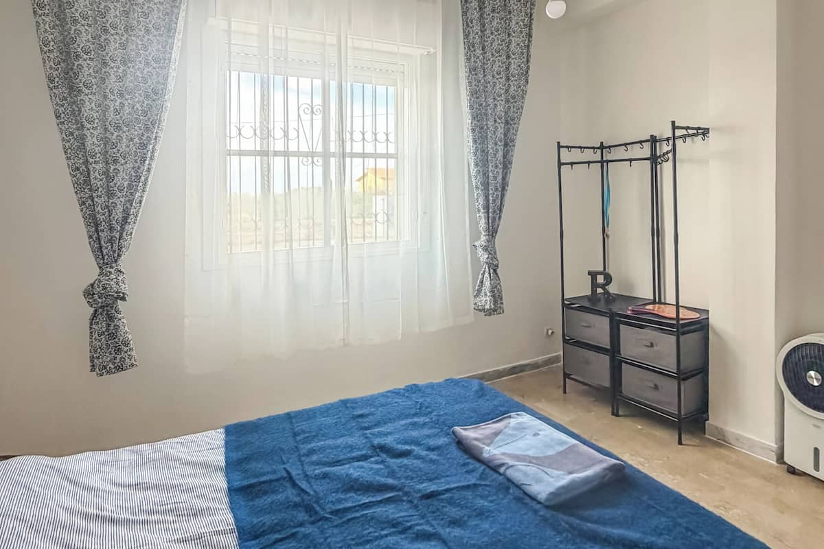 A bedroom with a bed, a desk, a chair, and a window with curtains.