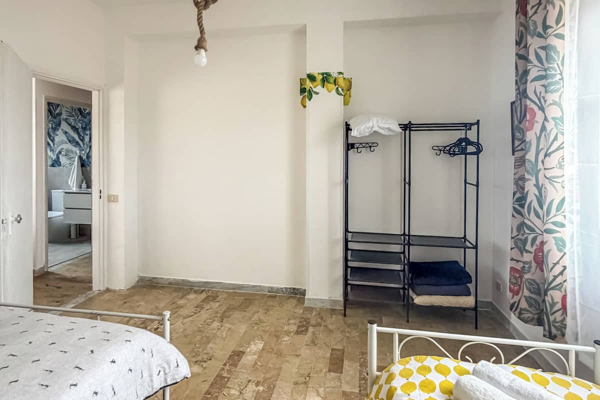 A bedroom with two beds, a bunk bed, a hanging light fixture, and a bathroom visible through an open door.