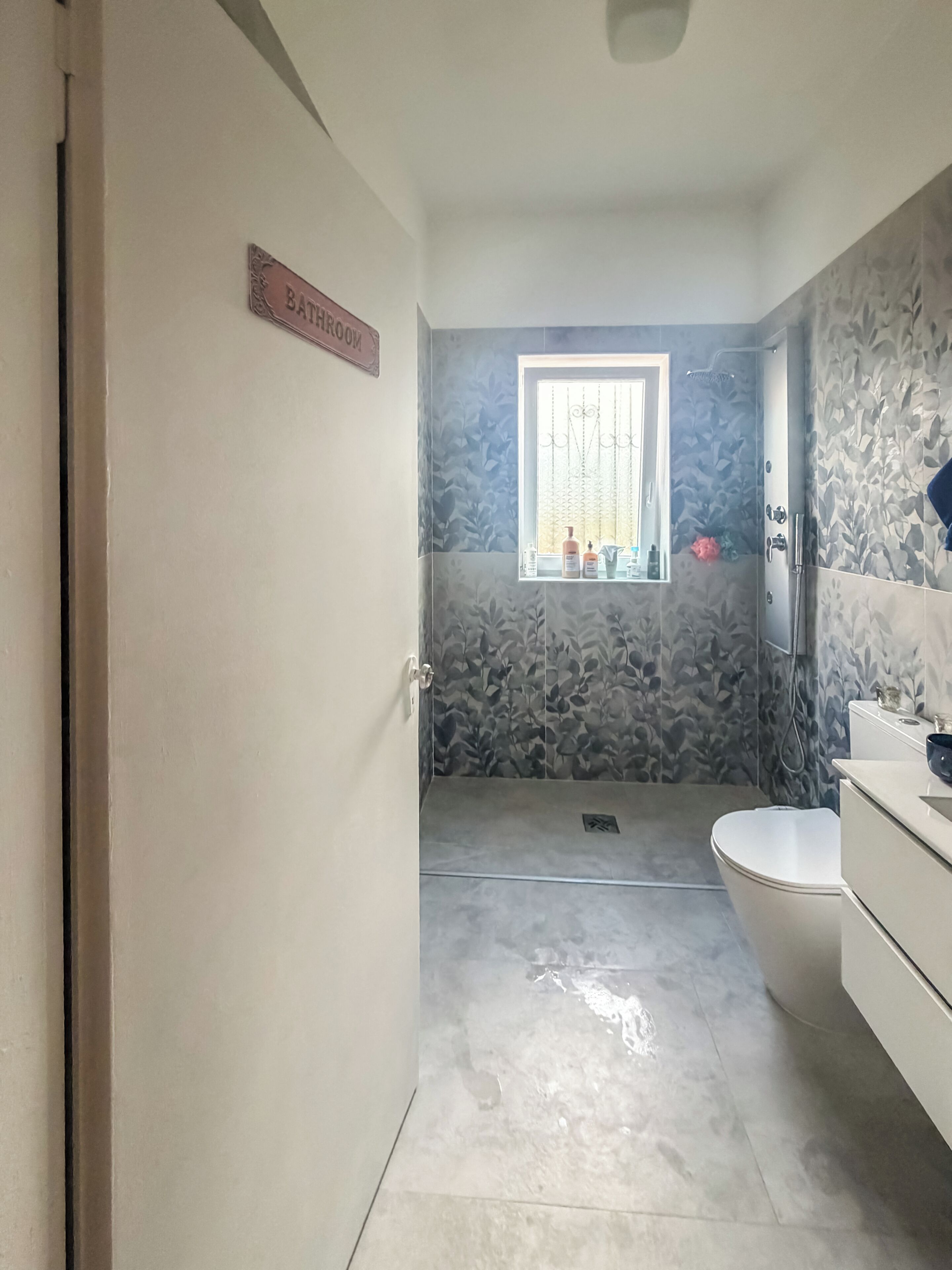 A bathroom with a shower, toilet, and a window with a curtain.