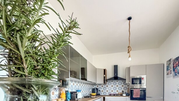 A modern kitchen with white cabinets, a central island, and a hanging light fixture. - Root and Rise (Caltagirone)