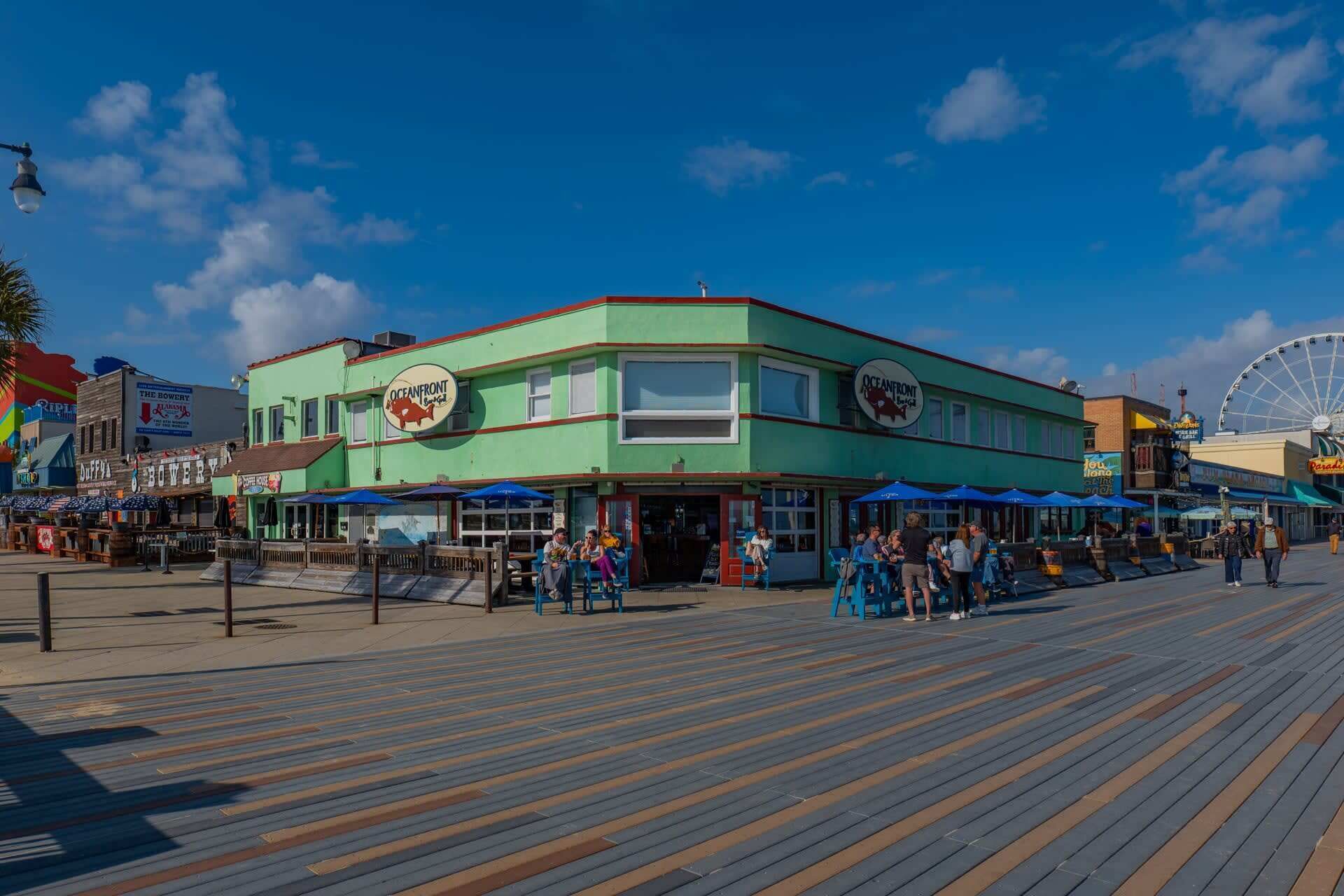 A waterfront boardwalk with a restaurant named 'Oceanfront Grill' and a Ferris wheel in the background.