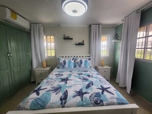 A bedroom with a bed, two bedside tables, a nightstand, a window, a ceiling light, and a green wardrobe.