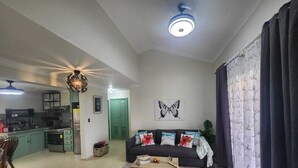 Sala de estar con sofá, mesa de centro y obras de arte. Se observa una zona de cocina con armarios y electrodomésticos.