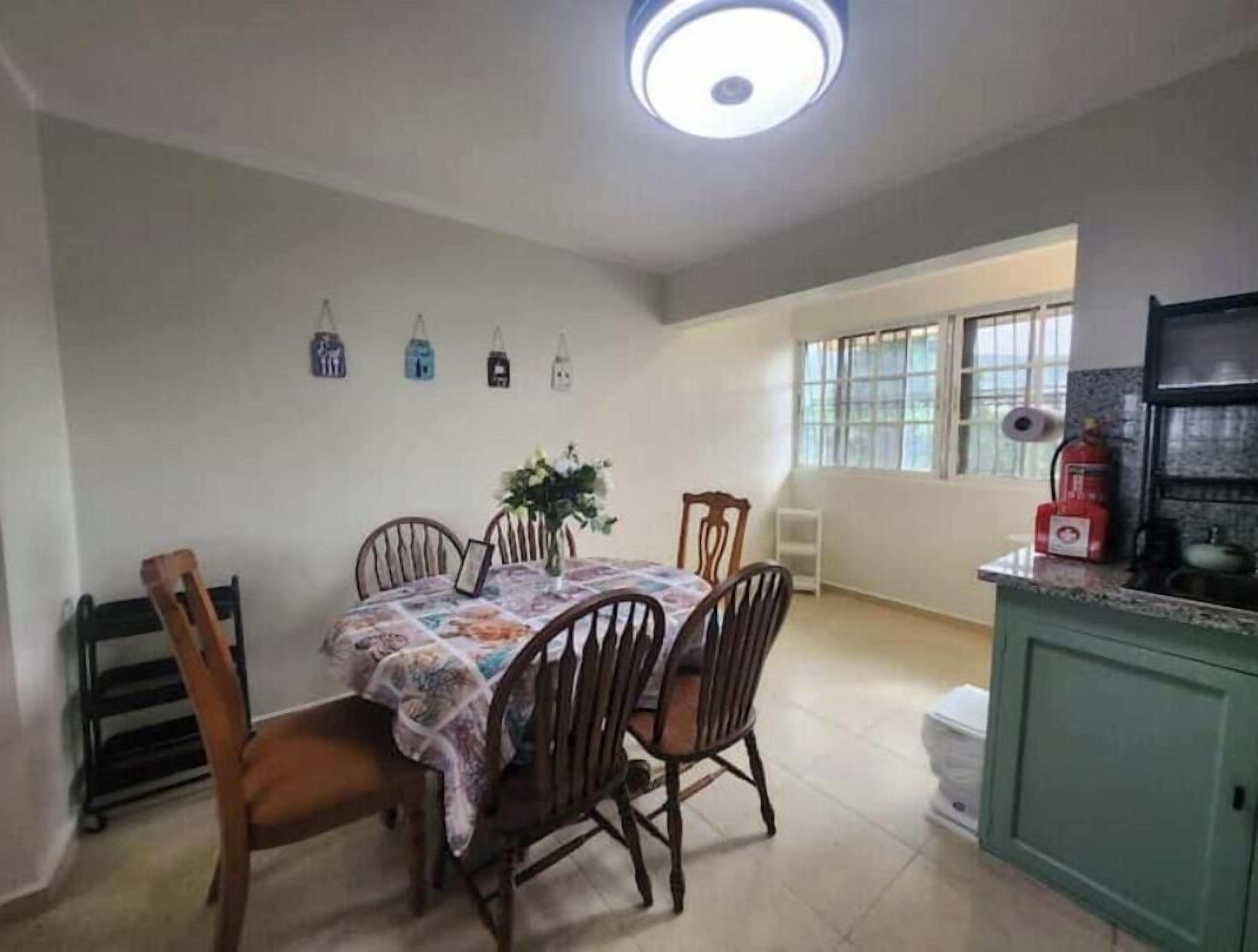A dining area with a table, chairs, a ceiling light, a window, and a kitchen counter.