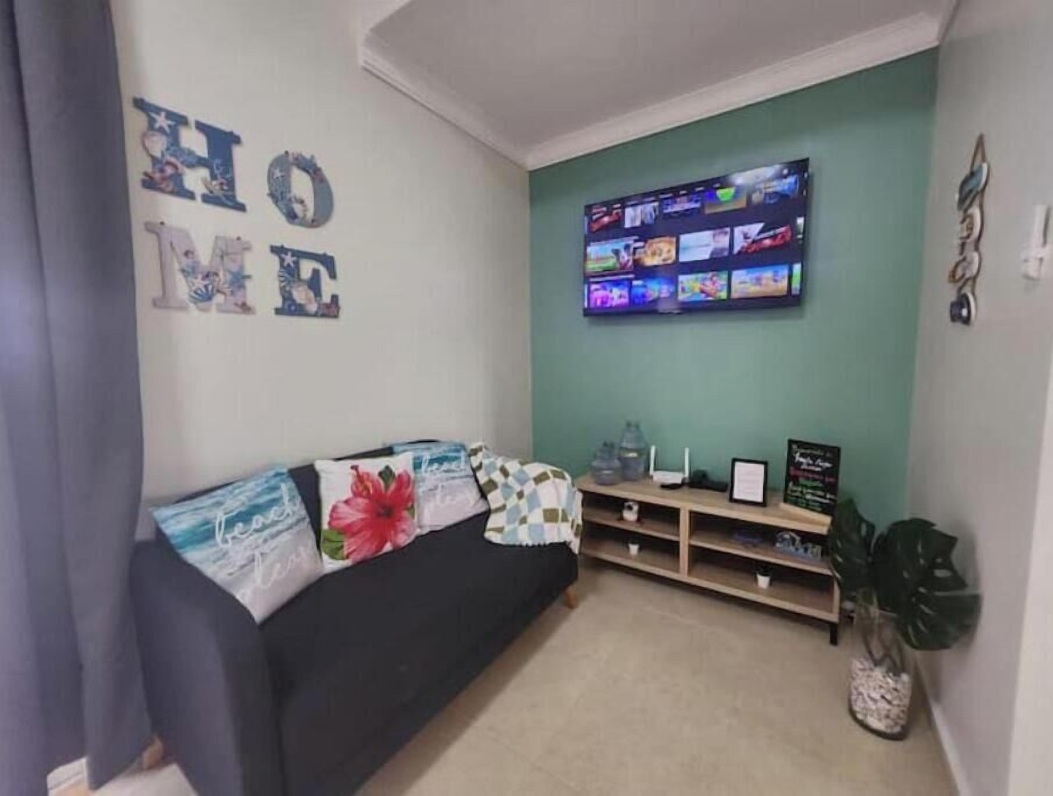A living room with a sofa, a flat-screen TV mounted on the wall, and a small shelf with items.