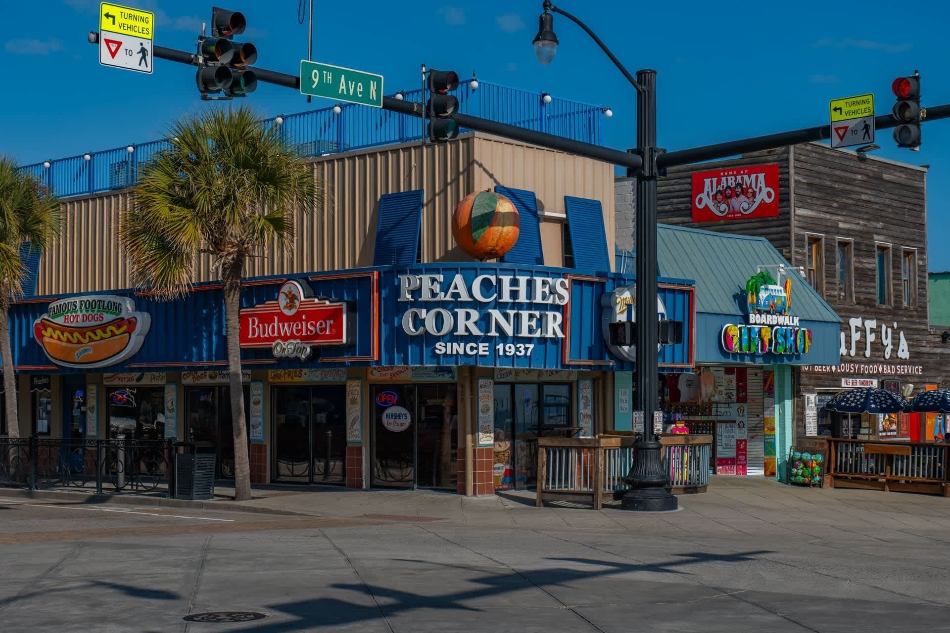 Una esquina de calle con un edificio que alberga un restaurante llamado 'Peaches Corner' y una tienda 'Boardwalk City Shop'.