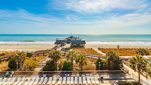 Een hotel aan het strand met een houten promenade, toegang tot het strand en een badwachterspost.