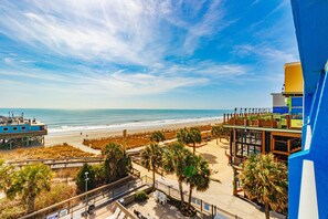 A beachside view with a boardwalk, palm trees, and a building with a blue facade. - Yachtsman S603B Studio (Myrtle Beach)
