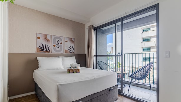 A bedroom with a bed, a window, and a balcony with a chair. - Your Code Liberdade (São Paulo)