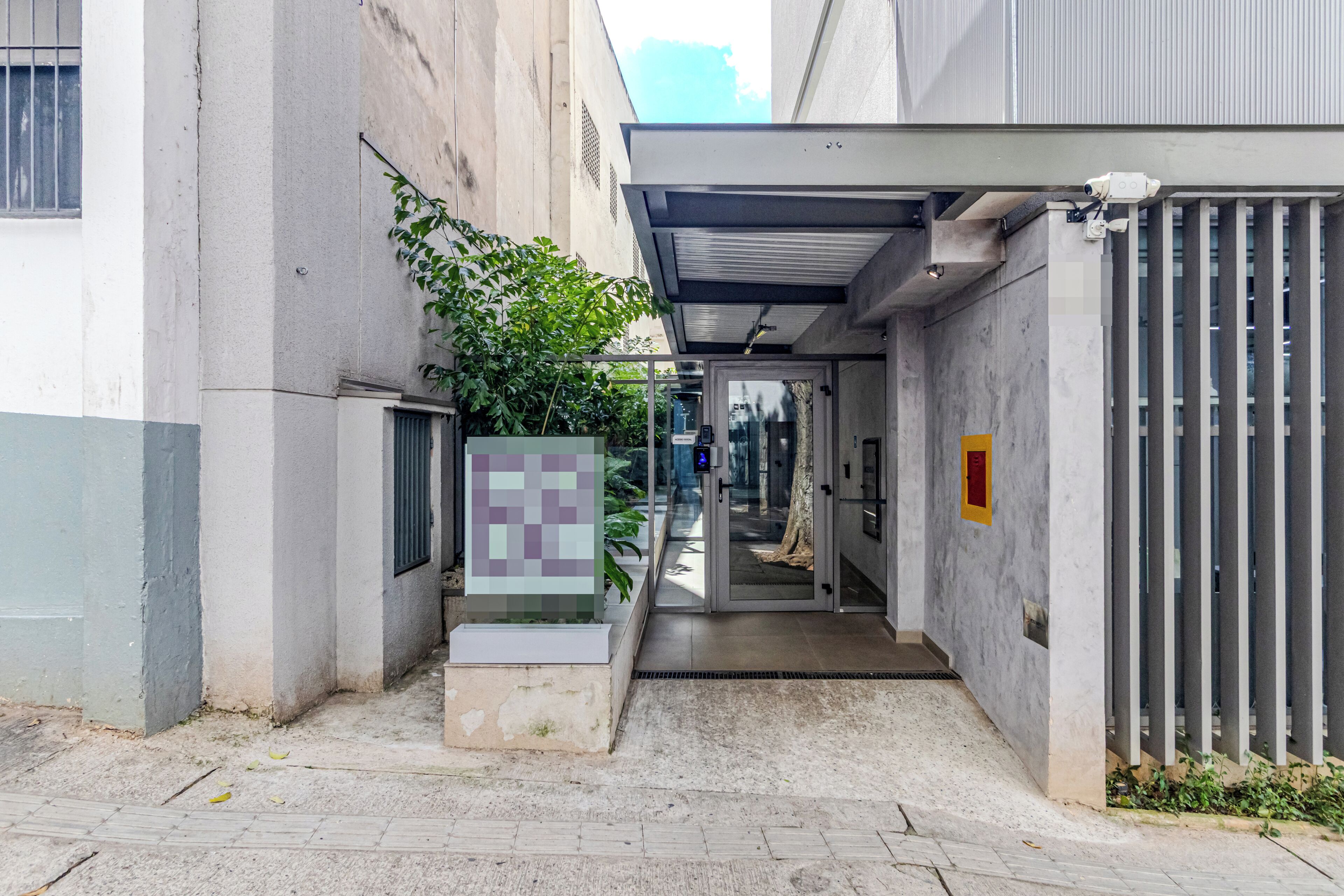 A narrow alleyway leading to a building entrance with a glass door, a security camera, and a metal gate.