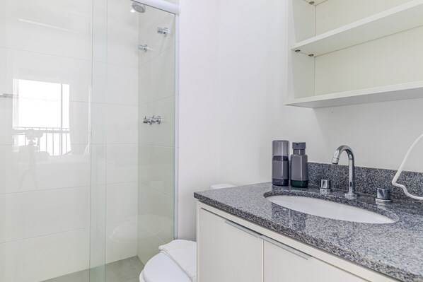 A modern bathroom with a glass shower enclosure, a granite countertop sink, and a white toilet. - Your Code Liberdade (São Paulo)