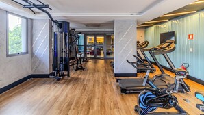 A gym with exercise equipment, a wooden floor, and large windows. - Your Code Liberdade (São Paulo)