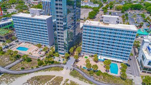 A high-rise hotel with multiple floors, a rooftop pool, and a landscaped courtyard with palm trees.