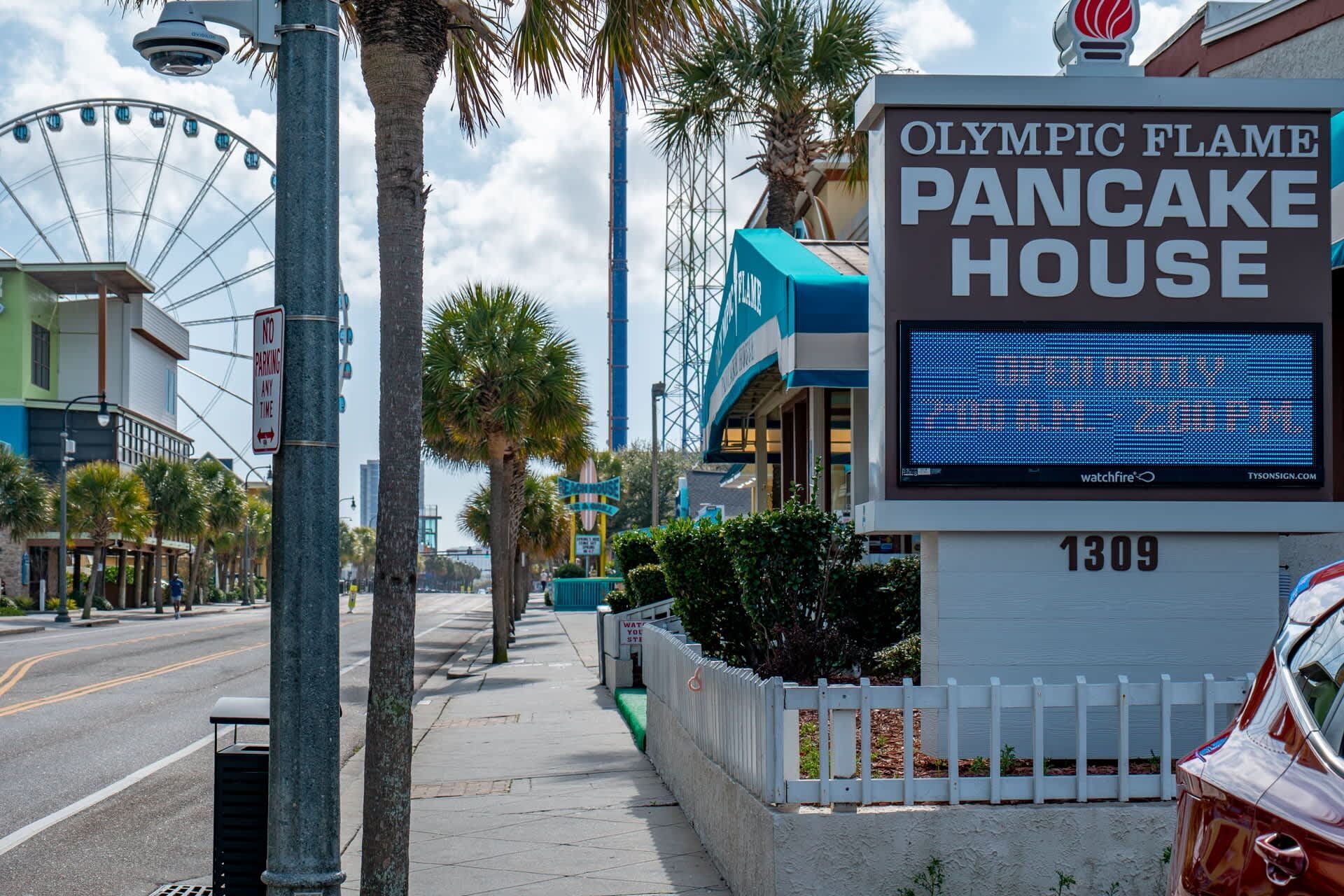 A street view with a sign for 'Olympic Flame Pancake House' and a Ferris wheel in the background.
