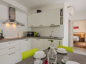 A modern kitchen with white cabinets, a microwave, and a coffee maker. There is a dining table with white plates and cups. - Antica Corte by Interhome (Arco)