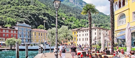 A waterfront promenade with buildings, a lamp post, and people dining at outdoor tables.