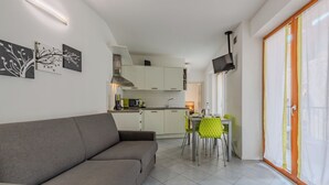 A modern living room with a sofa, a dining area with chairs, a kitchen with cabinets, and a TV mounted on the wall. - Antica Corte by Interhome (Arco)