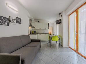 A modern living room with a sofa, a dining area with chairs, a kitchen with cabinets, and a TV mounted on the wall. - Antica Corte by Interhome (Arco)