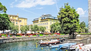 A waterfront area with boats docked, a stone wall, and buildings in the background. - Antica Corte by Interhome (Arco)
