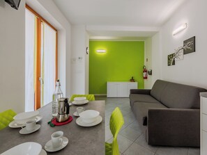 A modern living room with a grey sofa, a dining table with white plates and cups, and a green accent wall. - Antica Corte by Interhome (Arco)