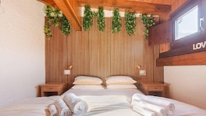 Camera da letto con parete in listelli di legno, letto con lenzuola bianche, due comodini e una finestra.