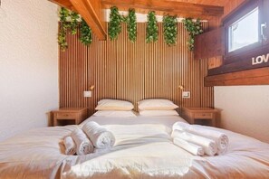 Een slaapkamer met een wand van houten latten, een bed met witte lakens, twee nachtkastjes en een raam.