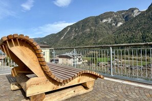 A wooden lounge chair with a curved backrest, positioned on a paved area with a metal railing in the foreground. - Val di Sole Apartment, with pets allowed (Trentino-Alto Adige)