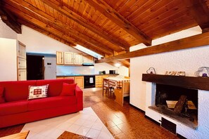 A cozy living room with a red sofa, a fireplace, and a kitchen in the background. - Val di Sole Apartment, with pets allowed (Trentino-Alto Adige)