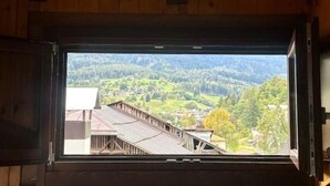 Una finestra con cornice in legno che si affaccia su un borgo e colline boscose.
