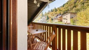 Un balcone in legno con tavolo e sedie, affacciato su un pendio con case.