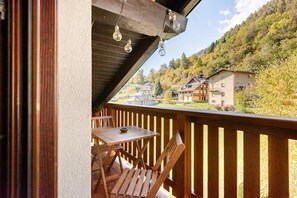 Een houten balkon met een tafel en stoelen, met uitzicht op een heuvel waar huizen staan.