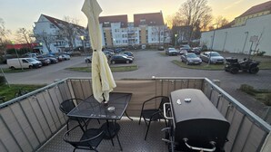 Un balcon équipé d’une table, de chaises, d’un barbecue et d’un parasol.
