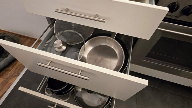 Une cuisine équipée d’un four encastré, d’une plaque de cuisson et d’un meuble à tiroirs contenant des casseroles et des poêles.