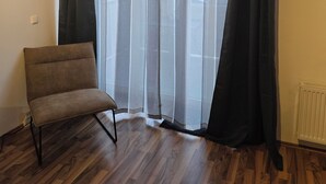 Une pièce avec un plancher en bois, une chaise marron, des rideaux légers et un radiateur.