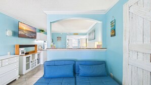 Una habitación con kitchenette, zona de comedor y espacio de descanso con cojines azules.