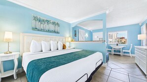 Habitación de hotel con cama, escritorio, silla, cómoda y un cuadro en la pared.
