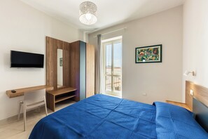 Une chambre avec un lit, une télévision, un bureau, un miroir et une vue sur le balcon.