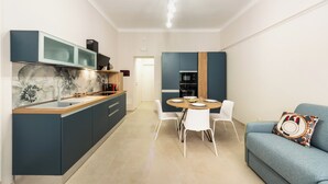 A modern kitchen with a marble backsplash, a dining area with a round table and chairs, and a blue sofa with a patterned pillow. - Casa Amarantia-Appartamento 2 (Noto)