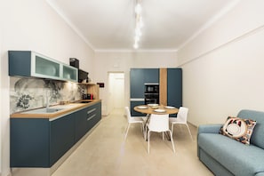 Une cuisine moderne avec un revêtement mural en marbre, un coin repas avec une table ronde et des chaises, et un canapé bleu agrémenté d’un coussin à motifs.