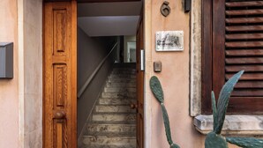 A wooden door leading to a staircase with a marble floor, a cactus plant, and a wall-mounted sign. - Casa Amarantia-Appartamento 2 (Noto)