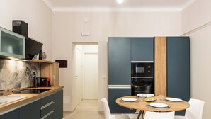 A modern kitchen with a dining area, featuring a wooden table, white chairs, and built-in appliances. - Casa Amarantia-Appartamento 2 (Noto)
