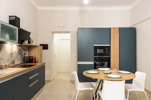 Une cuisine moderne avec un coin repas, comprenant une table en bois, des chaises blanches et des appareils électroménagers intégrés.