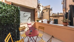 A balcony with a table and chairs, potted plants, and a view of neighboring buildings. - Casa Amarantia-Appartamento 2 (Noto)