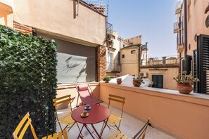 Un balcon avec une table et des chaises, des plantes en pot et une vue sur les bâtiments voisins.