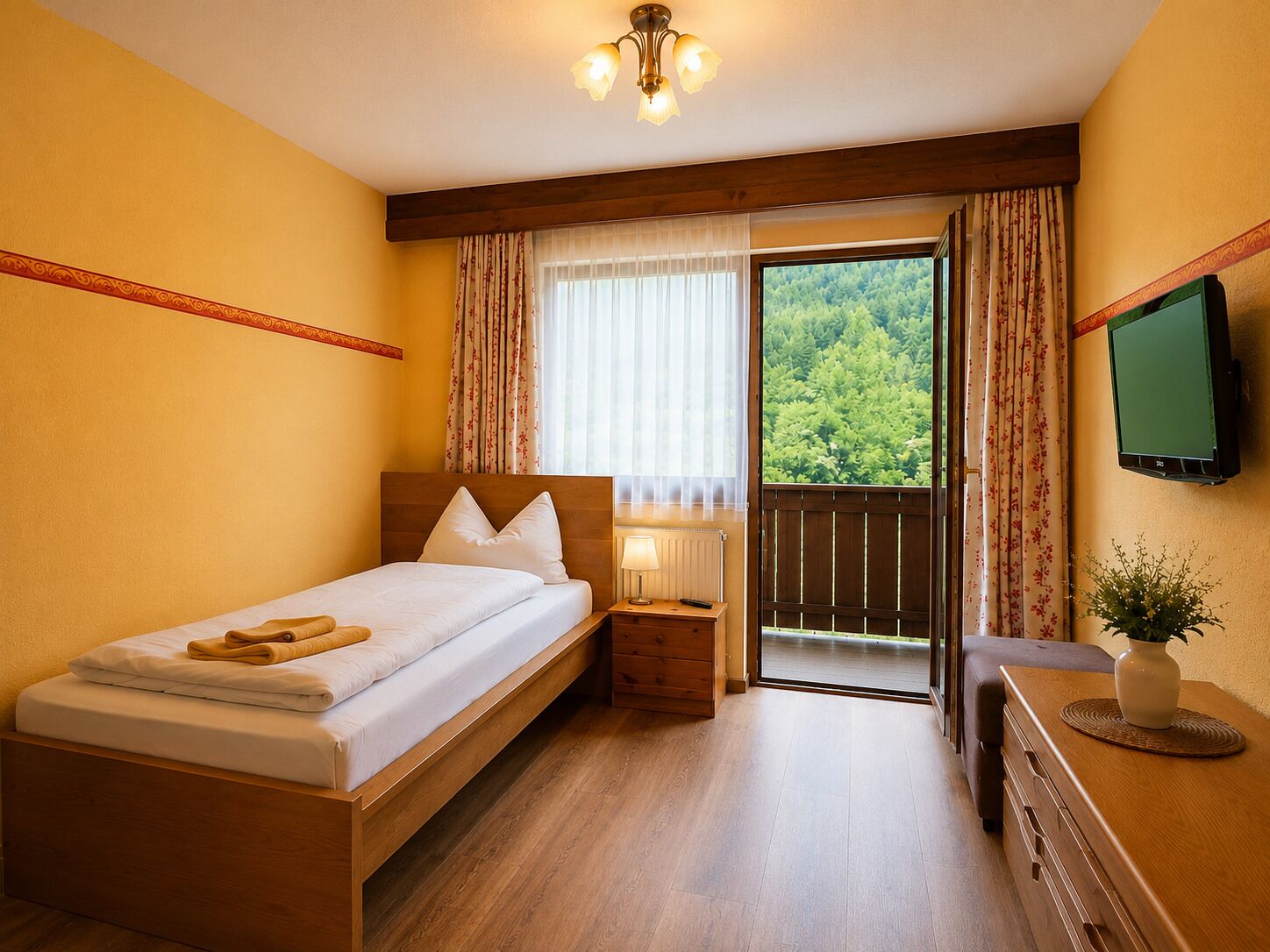 Ein Hotelzimmer mit Bett, Nachttisch, Lampe, Fernseher und Blick auf Grün durch eine Tür.