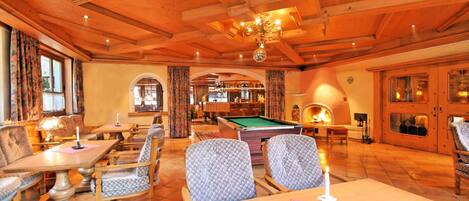 A cozy indoor setting with wooden beams, a billiards table, and comfortable seating areas.