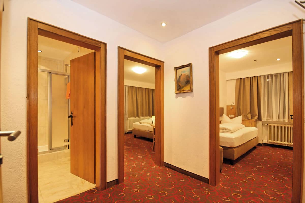 A hotel room with a red carpet, a bed, a bathroom with a shower, and a painting on the wall.