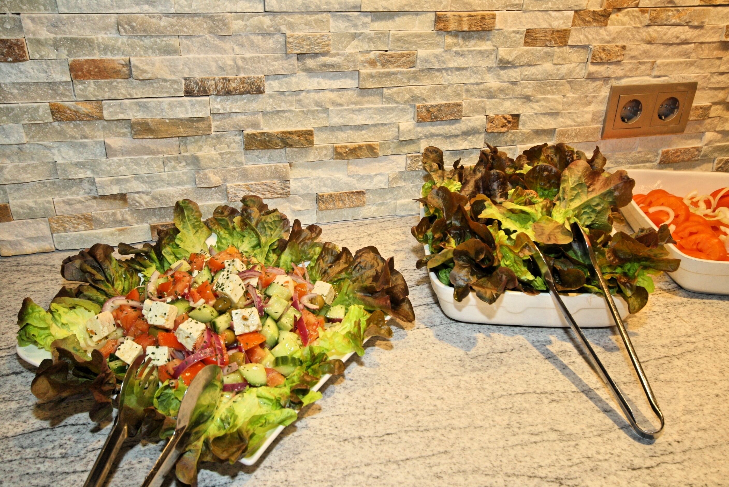 A kitchen counter with two bowls of salad, a stone wall, and a power outlet.
